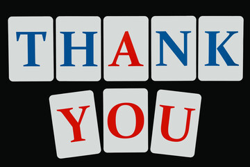 The word thank you composed of letters of blue and red color on white cards laid out on a black background
