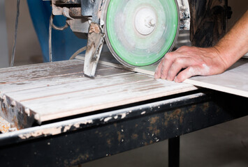 A worker is cutting a ceramic tile on a special electric wet water cutter saw machine. Maintenance repair in the flat. Renovation process.