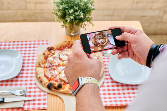Close-up of a man taking pictures of a pizza with his phone