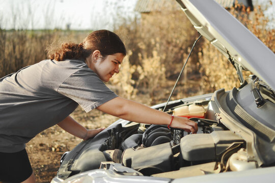 A woman repairs and troubleshoots a car outdoors on a bright sunny day