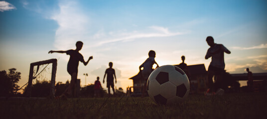 Action sport outdoors of kids having fun playing soccer football for exercise in community rural area under the twilight sunset sky. Picture with copy space