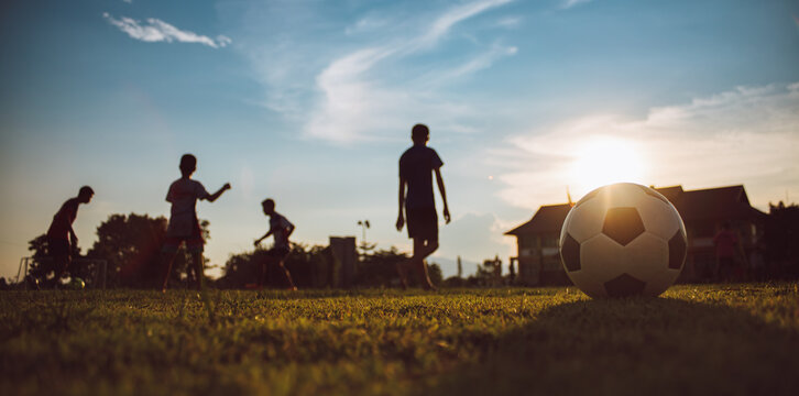 Action sport outdoors of kids having fun playing soccer football for exercise in community rural area under the twilight sunset sky. Picture with copy space