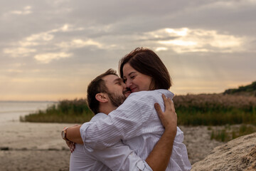 Couple in love hugs and smiles. They are on the seashore against the backdrop of cloudy clouds