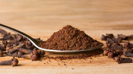 clove powder in a spoon with dry cloves around on a wooden table top, aromatic spice and herb,...
