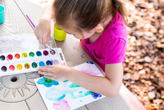 Child painting on paper outdoors on picnic table. Painting outside during the fall. Girl working on art project. 