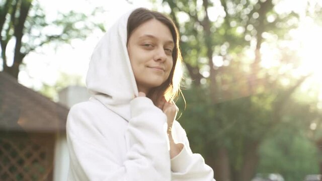Beautiful woman in white hoodie straightens her hair at sunset