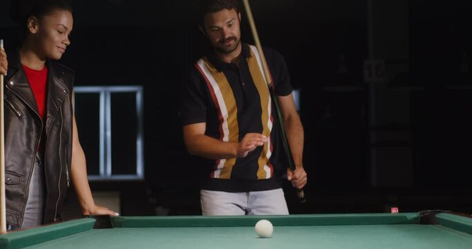 A man shows woman how to hold a cue and break a triangle in billiards