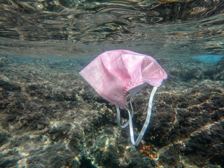 Concept of ocean pollution with a used one way facemask floating underwater, Pollution of ocean...