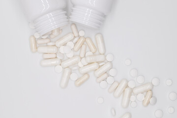 Heap of white pills and capsules, medicines, vitamins and useful food supplements scattered from sterile container on a white light background, flat lay with blank space top view