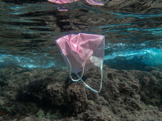 Concept of ocean pollution with a used one way facemask floating underwater, Pollution of ocean...