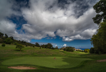 Fototapeta na wymiar Green with flag, clouds and see at Palheiro golf course on Madeira, Atlantic ocean, Portugal