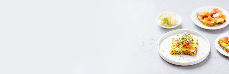 Flat lay top view of healthy sandwich with smoked salmon, cucumber, cream cheese and fresh microgreens alfalfa sprouts on white plate on gray concrete background. Healthy lifestyle. Growing sprouts