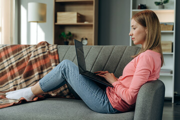 Enjoying time at home. Beautiful young smiling woman working on laptop while sitting in a big comfortable sofa at home