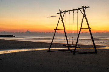 Fototapeta premium A large wooden swing on a sandy beach in the evening with a golden sky.