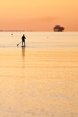 Fototapeta na wymiar a swimmer is rowing a board in a calm sea and sunrise