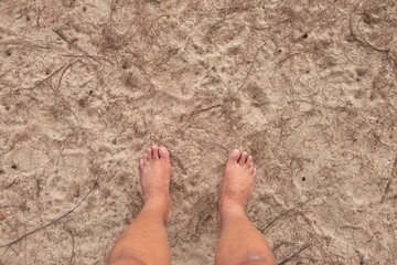 Two feet of an Asian man standing on the sandy shore.
