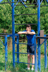 teenage boy exercising outdoors, sports ground in the yard, he posing at the horizontal bar, healthy lifestyle