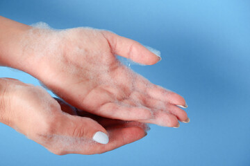 Bubble bath foam in woman's hands. Closeup woman's hand washing with soap on a blue background , selective focus. Practice good hygiene. Hygiene and health protection