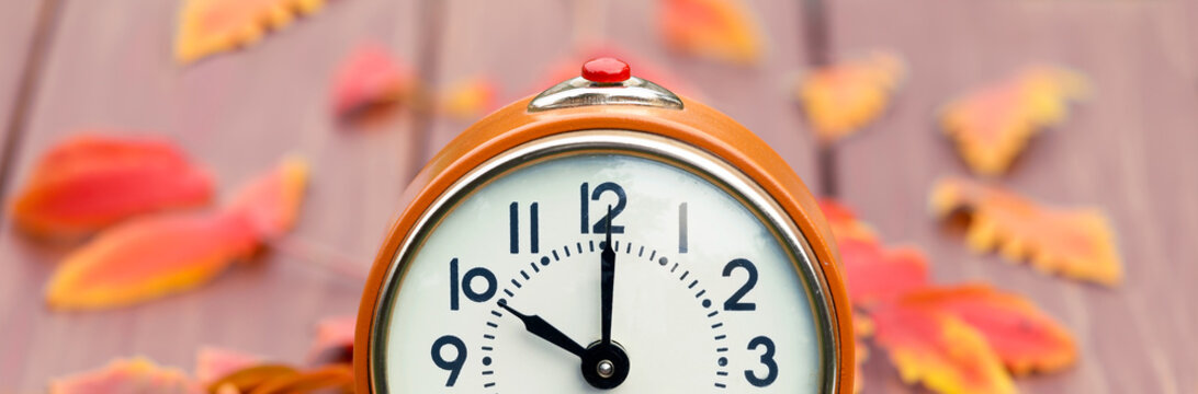 Orange clock and fall autumn leaves. Daylight saving time banner.