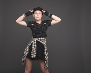 Young Woman in Black dress and Black Cap Poses in the Studio Before a Plain Gray Background