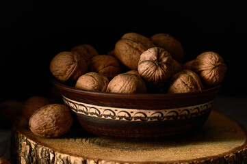 Грецкие орехи в глиняной миске. Цельный грецкий орех на древесном столе крупным планом

