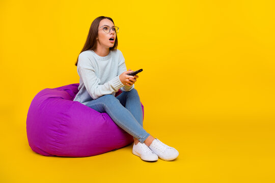 Full Body Photo Of Happy Amazed Shocked Young Woman Watch Tv Empty Space Remote Control Isolated On Yellow Color Background