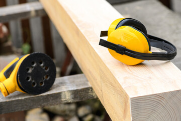 Protective earmuffs and eccentric orbital sander, grinder machine on a wooden surface