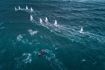 Regatta sailing ship yachts with white sails at opened sea. Aerial view of sailboat in windy condition.