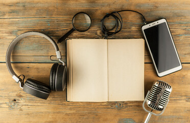 Black headphones with smarphone and open book are on the wooden table. Audio book concept. Distance...