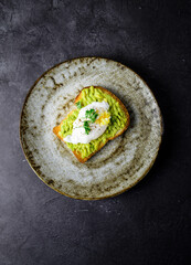 The burger with avacodo and poached egg for breakfast on the plate on the dark backgroubd. horizontal view.