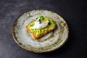The burger with avacodo and poached egg for breakfast on the plate on the dark backgroubd. horizontal view.