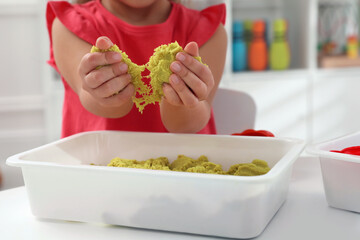 Little girl playing with bright kinetic sand at table indoors, closeup
