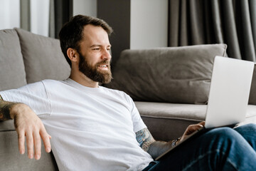 Bearded european man working with laptop while sitting on floor