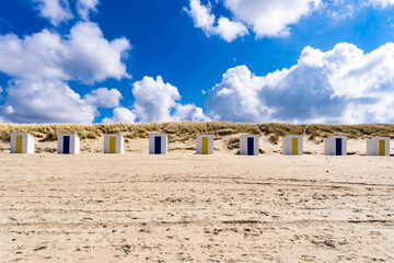 Naklejka premium Little beach cabins at a North Sea. White little houses on the deserted sand dunes of Netherlands with blue cloudy sky.