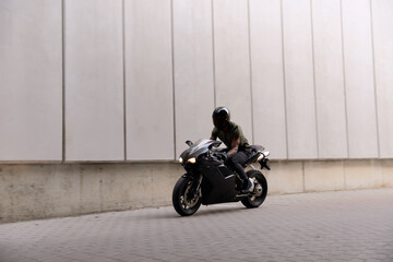 Naklejka na ściany i meble Black motorcycle biker in helmet on city street