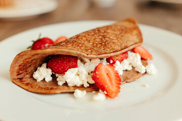 Pancakes with ricotta cheese and fresh strawberries on a white plate, close up.
