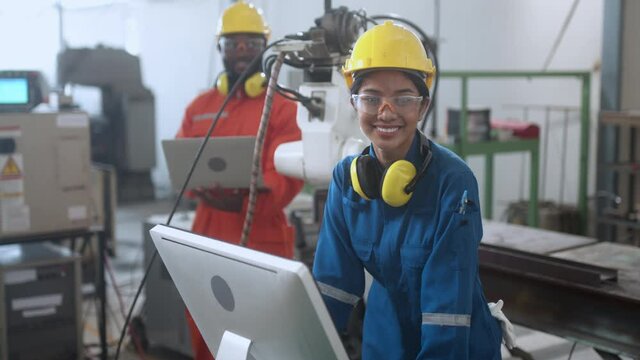 Female engineer smiling with confident while control programing data input for operate movement of welding robotarm at productine line in modern samrt technology factory industrial 4.0 ideas concept