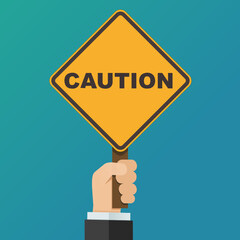 A hand holds up an orange diamond sign with the text Caution on a blue background (flat design)