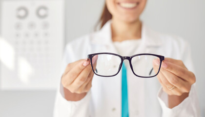 Smiling optician gives you new glasses. Happy doctor in white coat showing modern good quality eyewear. Optometry, prescription for glasses, eye health concept. Banner background, closeup, close up - obrazy, fototapety, plakaty