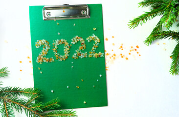 New Year 2022 on a green tablet with colored beads and fir branches on the background of the workspace. The concept of the beginning of success and the idea of a business task