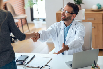 Obraz premium Handsome mature male doctor shaking hand with a patient in medical consultation.