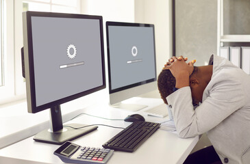 Unhappy, sad businesswoman or professional accountant sitting in front of multiple desktop computers, holding head in despair, waiting for new operating system to load or software update to install - obrazy, fototapety, plakaty