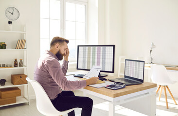 Stressed tired busy young businessman or corporate financial accountant sitting at working desk...