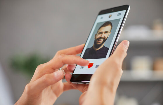 Love online: Woman using dating app and looking at pics of men on phone display. Young lady hits red heart icon and gives like to handsome guy on marriage website. Hands holding mobile in closeup