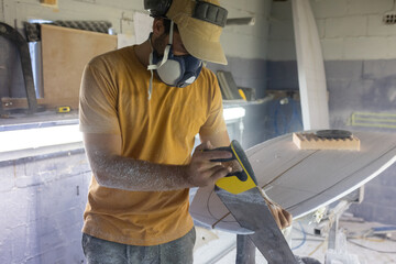 Surfboard making, woodworker wearing safety respirator sawing surfboard blank using handsaw