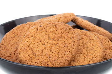 Several fresh oatmeal cookies in a black ceramic plate, close-up, isolated on white.