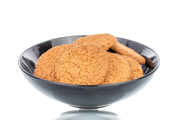 Several fresh oatmeal cookies in a black ceramic plate, close-up, isolated on white.