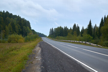 Fototapeta na wymiar A shallow two-lane highway in Russia in the Urals, passing through the forest. Landscape shot in cloudy daytime.