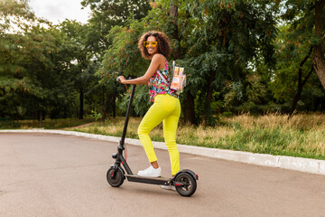 young stylish black woman having fun in park riding on electric kick scooter