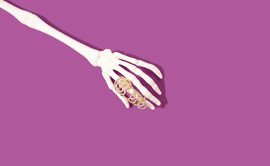 Skeleton hand with beauty ring on violet background. Bizarre concept.